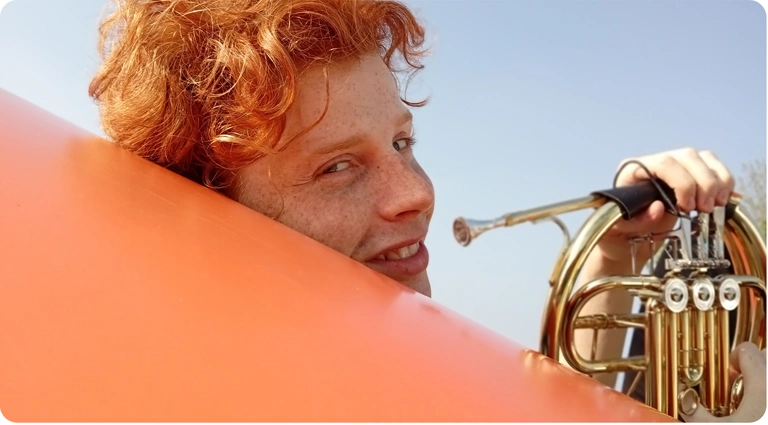 Mężczyzna o rudych włosach trzymający instrument dęty, portret wykonany aparatem Redmi 15C.