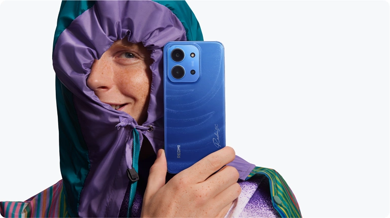 Uśmiechnięty osoba w kolorowej kurtce prezentująca niebieski telefon Redmi 15C w dłoni