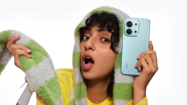 Młoda osoba w żółtej bluzie i w zielono-szarym szaliku trzymająca zielony telefon Redmi 15C w pozycji poziomej