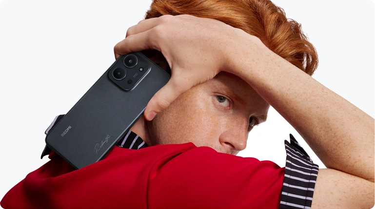 Mężczyzna w czerwonej koszulce prezentujący czarnego smartfona Redmi 15C trzymanego nad ramieniem