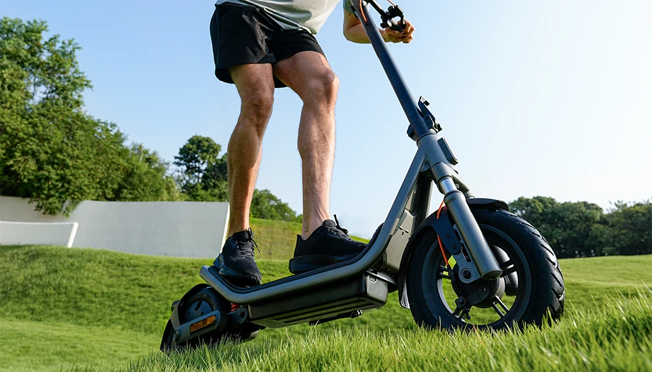 Widok boczny Xiaomi Electric Scooter 6 z użytkownikiem jadącym po zielonym terenie.