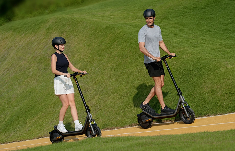 Dwie osoby jadące na Xiaomi Electric Scooter 6 po ścieżce w parku, w kaskach ochronnych