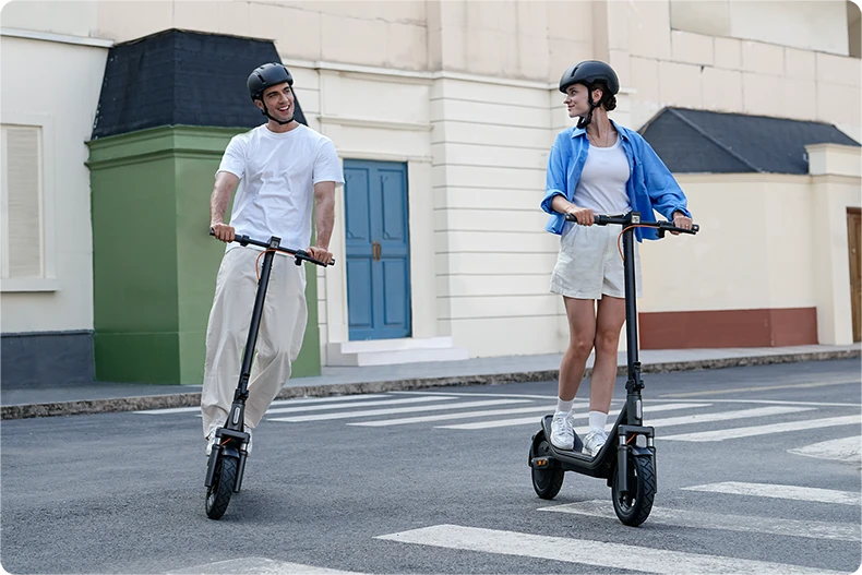 Dwie osoby jadące na Xiaomi Electric Scooter 6 po miejskiej ulicy, w kaskach ochronnych